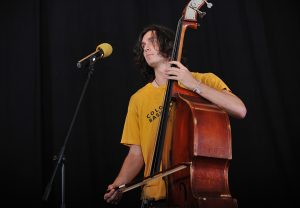 Man alone on stage playing an upright bass